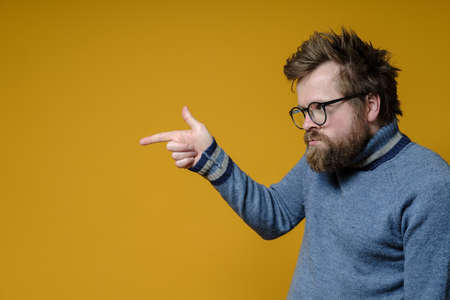 Offended, embittered shaggy, bearded man with glasses and a sweater points finger at someone with displeasure. Copy space.の写真素材