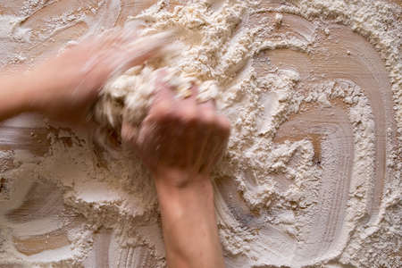 Hands knead the dough, on a wooden table. Photo in motion, blur. Top view.の写真素材