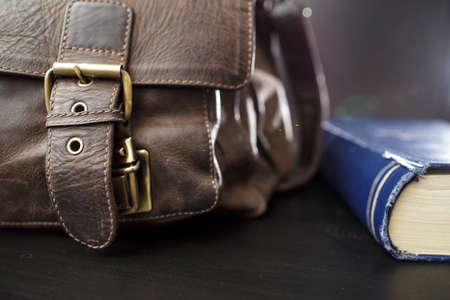 Old leather briefcase with metal buckles and a closed book lying on the table. Education concept.の写真素材
