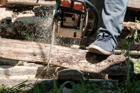 Male hands sawing old boards for firewood with a professional chainsaw, in a village yard. Winter preparation concept. Lifestyle.の写真素材