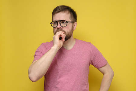Attractive bearded man puzzled, he thoughtfully looks away, covering mouth with hand. Yellow...