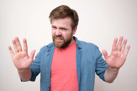 Disgruntled bearded man makes a stop gesture with his palm, a gesture of protection and looks...