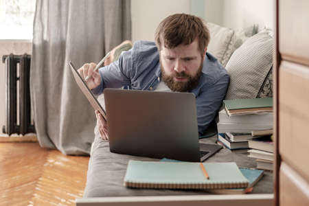 Student lies on a couch, looks intently at a laptop. Concept of distance online education.の写真素材