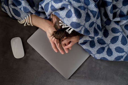 Woman covered with a plaid fell asleep on the laptop, she was tired of work and decided to rest.の写真素材