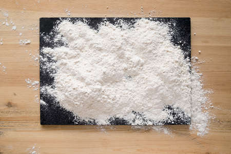 Flour sprinkled on a slate cutting board that is on a wooden table. Copy space.の写真素材