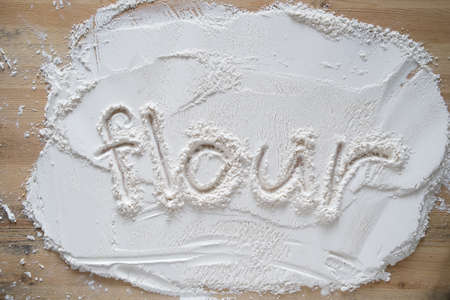 The handwritten word flour is written on milled, sifted wheat sprinkled on a wooden table.の写真素材