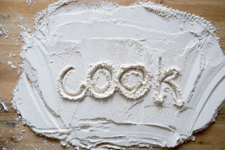 The handwritten word cook is written on flour sprinkled on a wooden table.の写真素材