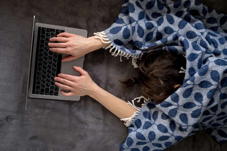 A woman covered with a plaid fell asleep working with a laptop, lying on a soft couch at home.の写真素材