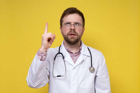 Strange doctor raised index finger and eyes upward, he thought and tried to remember something. Yellow background.の写真素材