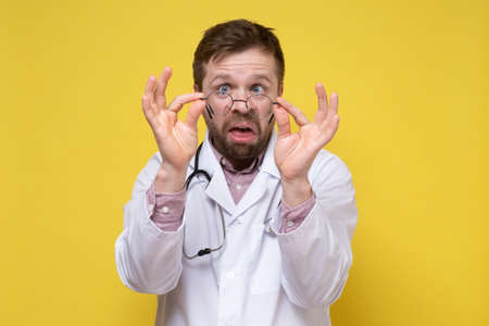 Bizarre doctor with poor eyesight has taken off glasses and is looking, with a stupid expression on face. Yellow background.の写真素材