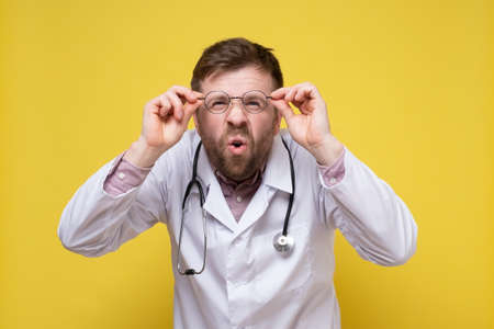 Funny doctor with poor eyesight holds glasses in hands and tries to see something, with a surprised expression on face.の写真素材
