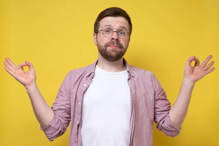 Funny bearded man with glasses meditates, trying to find harmony and balance, he connects thumb and forefinger and looks benevolent.の写真素材
