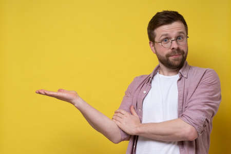 Attractive Caucasian man insistently offers something, he makes a hand gesture to the side and looks into the camera. Copy space.の写真素材