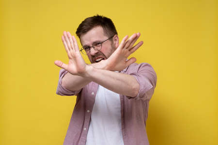 Caucasian man wearing glasses and casual clothes makes stop gesture by raising crossed arms and looking with disgust and fear.の写真素材