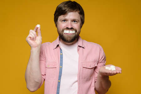 Funny man put sugar lumps in mouth as if it were teeth and smiles. Yellow background.の写真素材