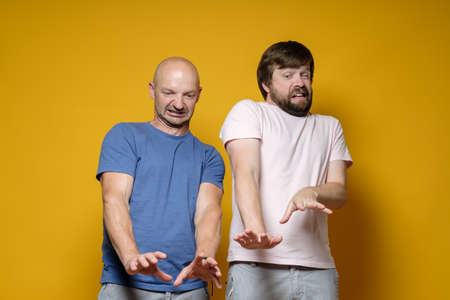 Two frightened, surprised men make a stop gesture with their arms outstretched and look down with disgust and dislike.の写真素材
