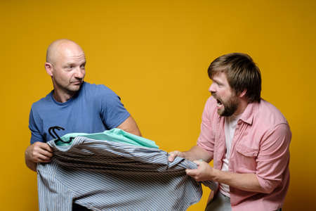 Two men grabbed one thing at the sale, they scold and do not yield to each other. Shopping. Yellow background.の写真素材