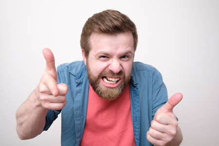 Strange bearded man makes a gesture with hands like it a gun and bares teeth. White background.の写真素材