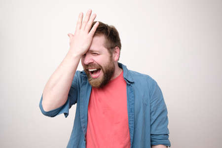 Cheerful, laughing bearded man is glad that he remembered something important, he holds hand on forehead and rejoices.の写真素材