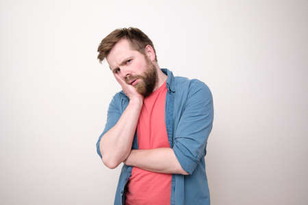 Caucasian man is upset or has a toothache, he holds hand on cheek and looks sad. White background.の写真素材