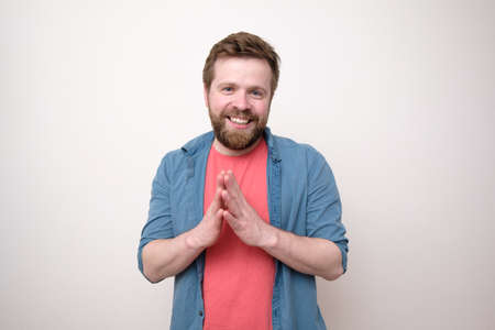 Smiling bearded man calmly and confidently looking at the camera with palms together. Isolated, white background.の写真素材