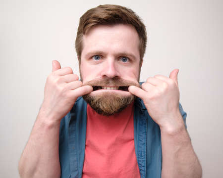 Whimsical bearded man made a funny, frightening grimace, he put fingers in his mouth and holds it open, looking at the camera.の写真素材