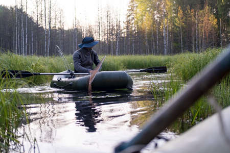 Fisherman in a hat on an inflatable boat prepares for fishing in the strait between the lakes, at dawn.の写真素材