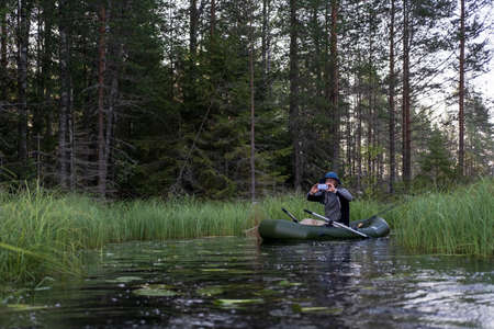 Fisherman on an inflatable boat photographs a beautiful morning landscape on a smartphone camera, against the background of a forest.の写真素材