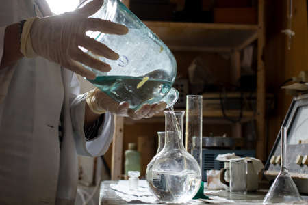 Scientist in a white coat and gloves conducts an experiment, he pours liquid from one flask to another, in the laboratory.の写真素材