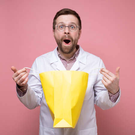Amazed, happy doctor holding a package of surprise, he happily looks into the camera with big eyes and mouth open.の写真素材