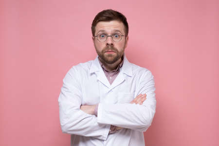 Young doctor in round glasses and a white coat is very surprised and bewildered, he crosses arms and looks with big eyes.の写真素材