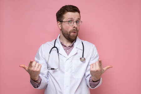 Satisfied, cute doctor with a stethoscope around neck makes a gesture with hands and fingers and looks at the camera in surprise.の写真素材