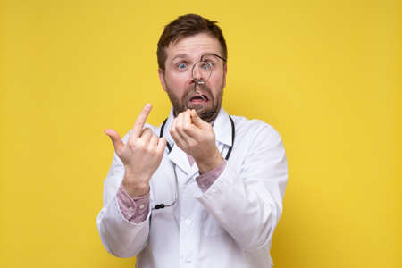 Upset, surprised doctor has taken off glasses and points at them with a foolish expression on face. Yellow background.の写真素材