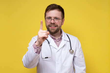 Calm, benevolent doctor raised his index finger up, he found a solution to the problem and is very happy. Yellow background.の写真素材