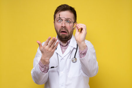 Poorly seeing doctor took off glasses and looked at them in bewilderment with a stupid expression on face. Yellow background.の写真素材