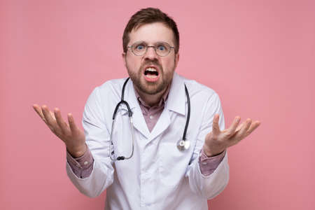 Furious, surprised doctor makes a questioning and bewildered gesture with hands and looks at the camera.の写真素材