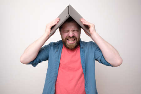 Man is stressed, he put the laptop on head and bares teeth in frustration. White background.の写真素材