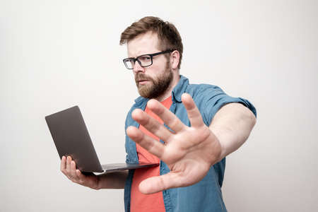 Stern man holds a laptop in one hand, and puts the other forward showing a stop gesture and looks sternly at the camera.の写真素材