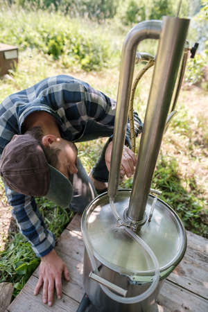 Focused man makes an alcohol mashine in a village courtyard, on a summer day. Preparation of an alcoholic beverage.の写真素材