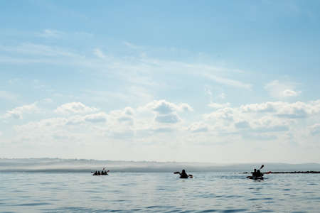 Silhouettes of three kayaks with tourists floating on the lake against the horizon. Leisure activities and sports.の写真素材