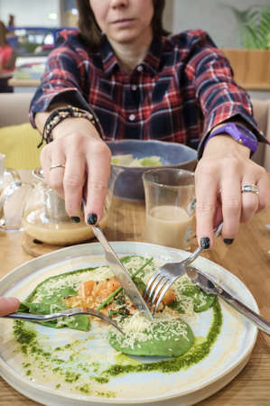 Hungry, serious woman with a fork and a knife eats food from someone else plate.の写真素材