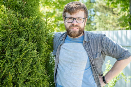 Satisfied male gardener hugs the thuja he raised and smiles sweetly in the garden on a summer day.の写真素材