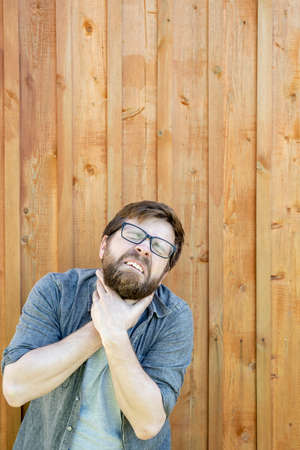 Man with glasses suffers from severe sore throat or suffocation, he holds neck with hands and suffers. Copy space.の写真素材