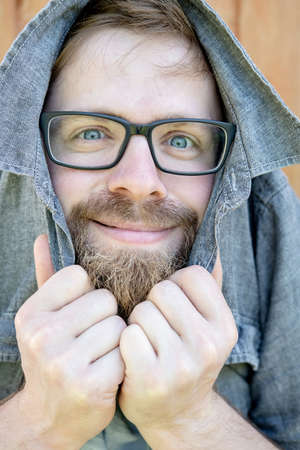 Bizarre, cute bearded man with glasses covers head with a shirt and looks into the camera. Close-up.の写真素材