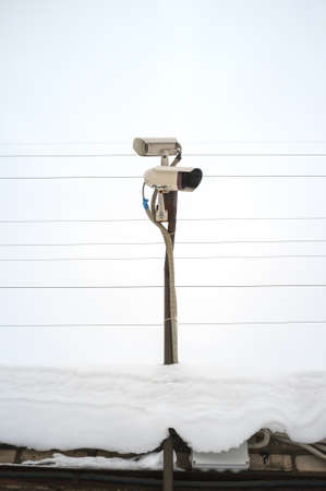 Two CCTV cameras stand on a snow-covered roof against a sky. Security concept.の写真素材