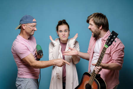 Men accuse each other of excessive noise, one is holding a guitar, the other is a drill, a shocked woman is standing between them.の写真素材