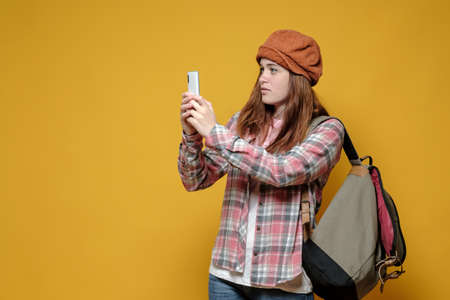 Attractive tourist with a city backpack takes pictures of landmarks on her smartphone. Leisure. Copy space. Yellow background.の写真素材