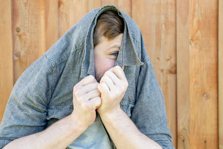 Funny man, put a shirt on head and peeks with one eye, against the background of a wooden wall.の写真素材