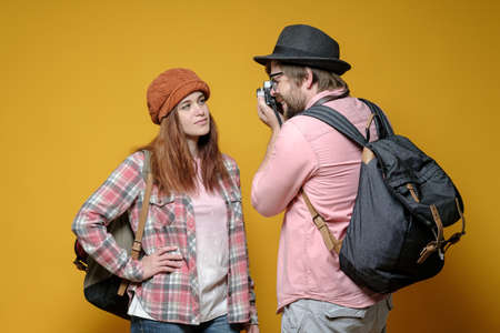 Man photographing woman. Tourist with a backpack in the city tour, walk and take pictures on the memory, isolated on a yellow background.の写真素材
