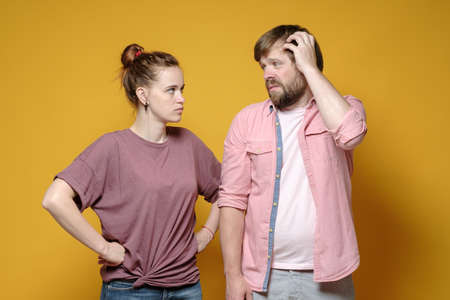 Woman looks sternly and angrily at a man who looks guilty. Domestic violence concept. Abuse. Yellow background.の写真素材